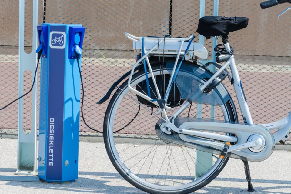 An e-bike is plugged into a public charger on a sunny day.